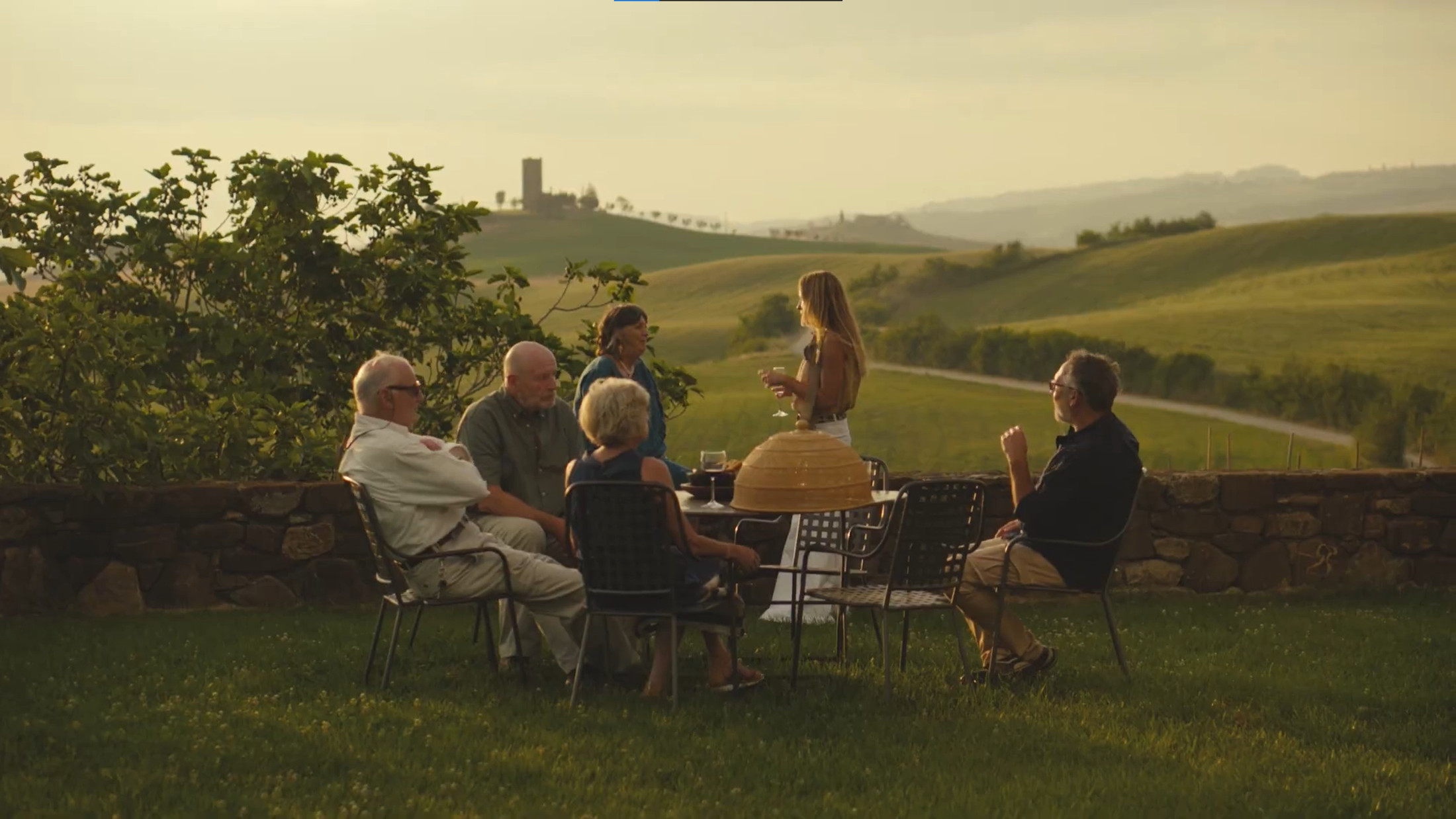 A group of people around a table on the lawn enjoying the sunset on a Tuscan hillside