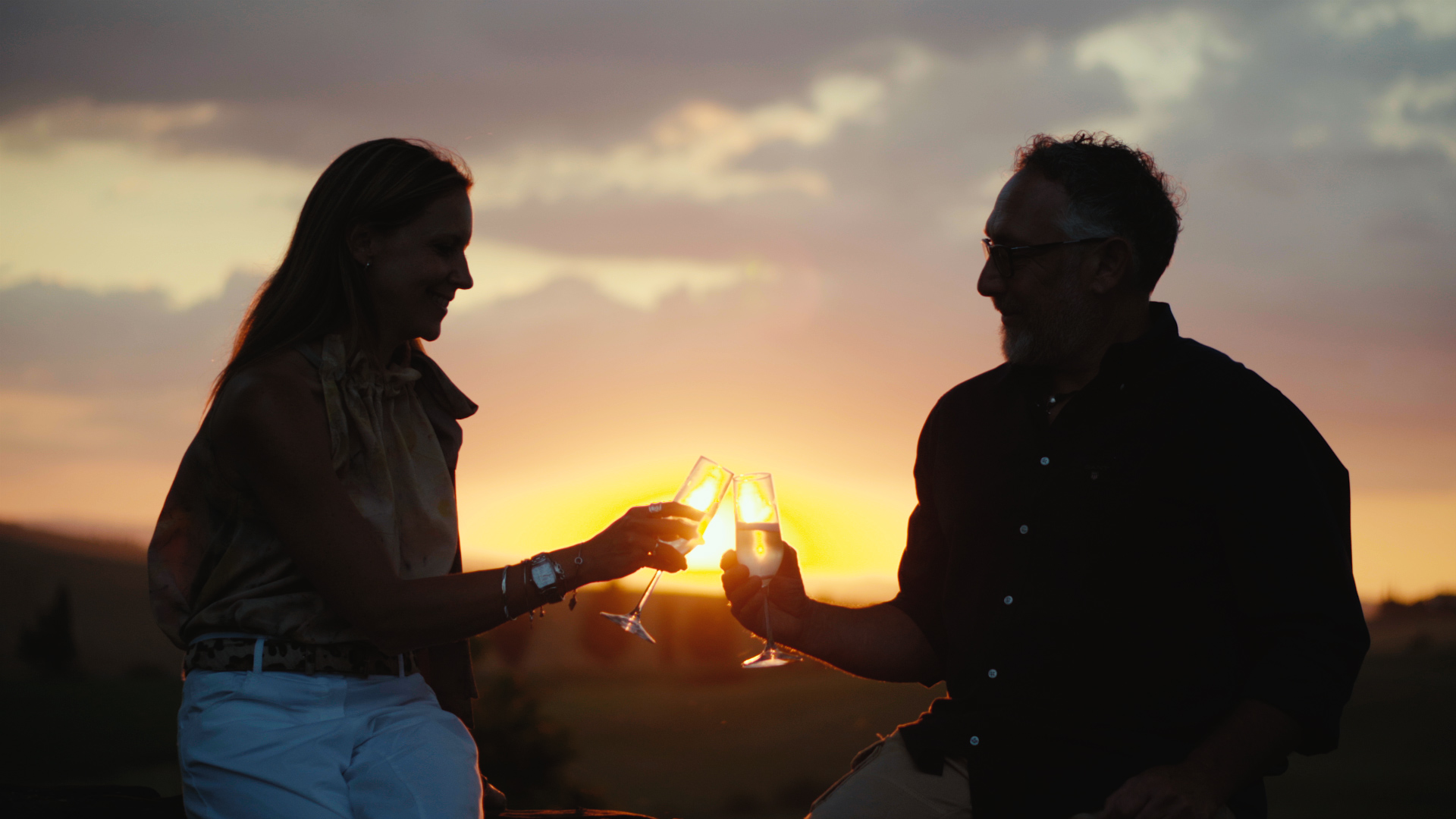 Man and woman raising wine glasses to toast at sunset
